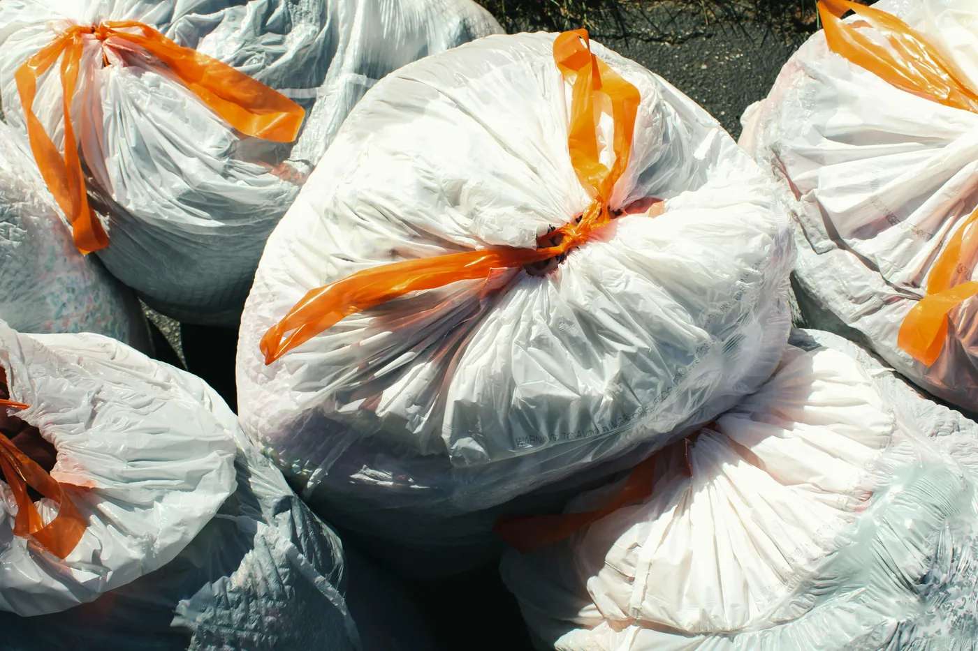 Multiple white trash bags tied with orange ribbons ready for curbside collection