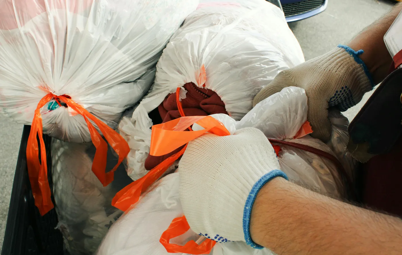 Gloved hands tying off white trash bags during garbage removal